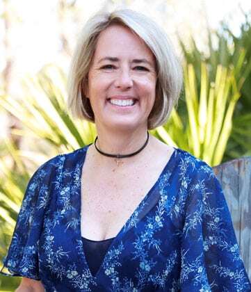 Woman with short gray hair smiling outdoors, wearing a blue floral top.