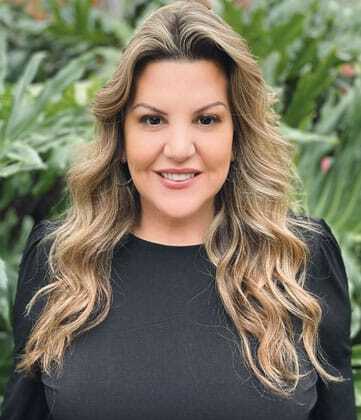 Professional headshot of a smiling woman with long wavy hair wearing a black top.