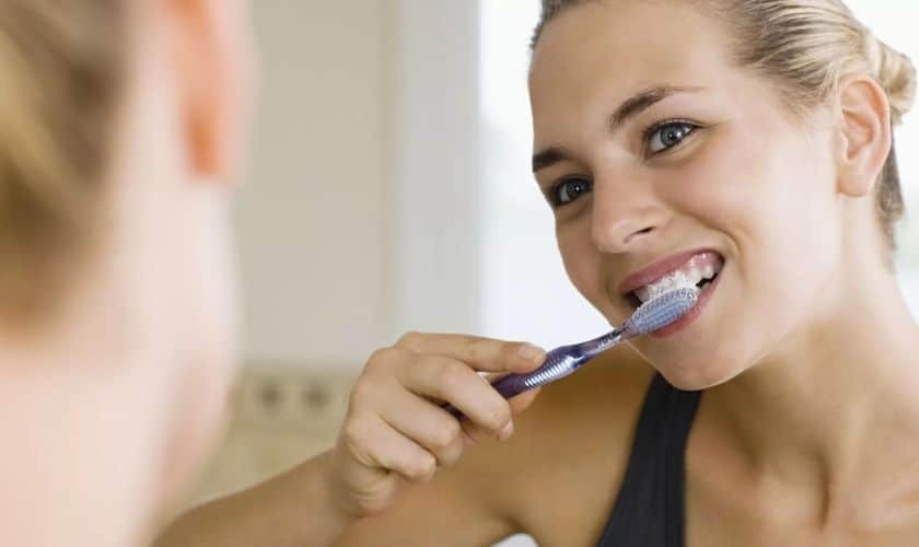 Woman brushing her teeth with a toothbrush, demonstrating proper daily oral hygiene.