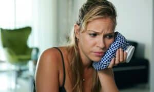 Woman holding ice pack to her cheek, experiencing dental pain or swelling.