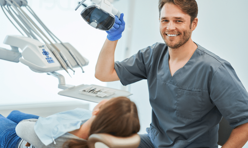 Smiling dentist holding dental mirror above patient in treatment chair at Niceville dental office.