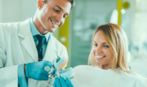 Male cosmetic dentist showing dental model to smiling female patient in modern dental office.