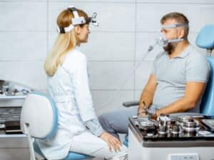 Dentist fitting sleep apnea oral appliance to patient in treatment room.