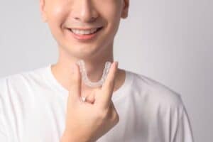 Young man holding clear Invisalign aligner, smiling while displaying orthodontic treatment option.