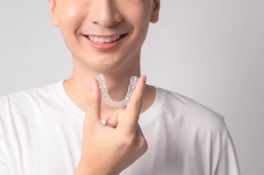 Young man holding clear Invisalign aligner, smiling while displaying orthodontic treatment option.