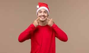 Man in Santa hat pointing to his smile, promoting holiday dental health.