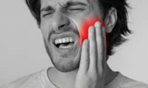 Man holding jaw in pain with red highlight indicating severe gum infection or dental emergency.