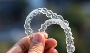 Clear dental aligner retainers held in hand, showing proper Invisalign aftercare and maintenance.