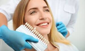 Dentist showing patient tooth shade guide for smile color matching during cosmetic dental consultation.