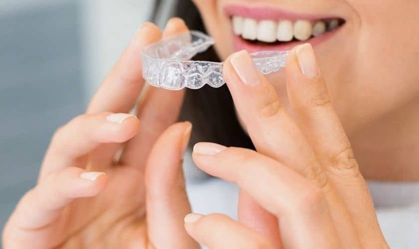 Woman inserting clear Invisalign aligners to straighten teeth as part of her daily orthodontic treatment.