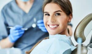 Smiling patient in dental chair with dentist holding instruments during oral health treatment.