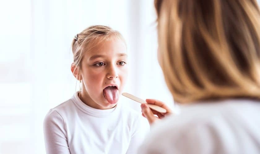 Young girl sticking out tongue for dental examination by healthcare provider.