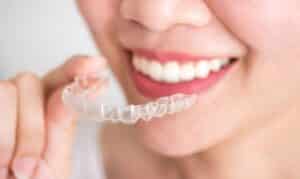 Woman holding clear Invisalign aligner tray while smiling, showing teeth alignment treatment option.
