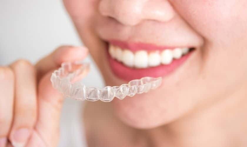 Woman holding clear Invisalign aligner tray while smiling, showing teeth alignment treatment option.