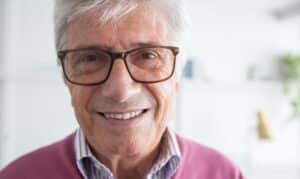 Smiling older man with glasses wearing a pink sweater in a dental office setting.