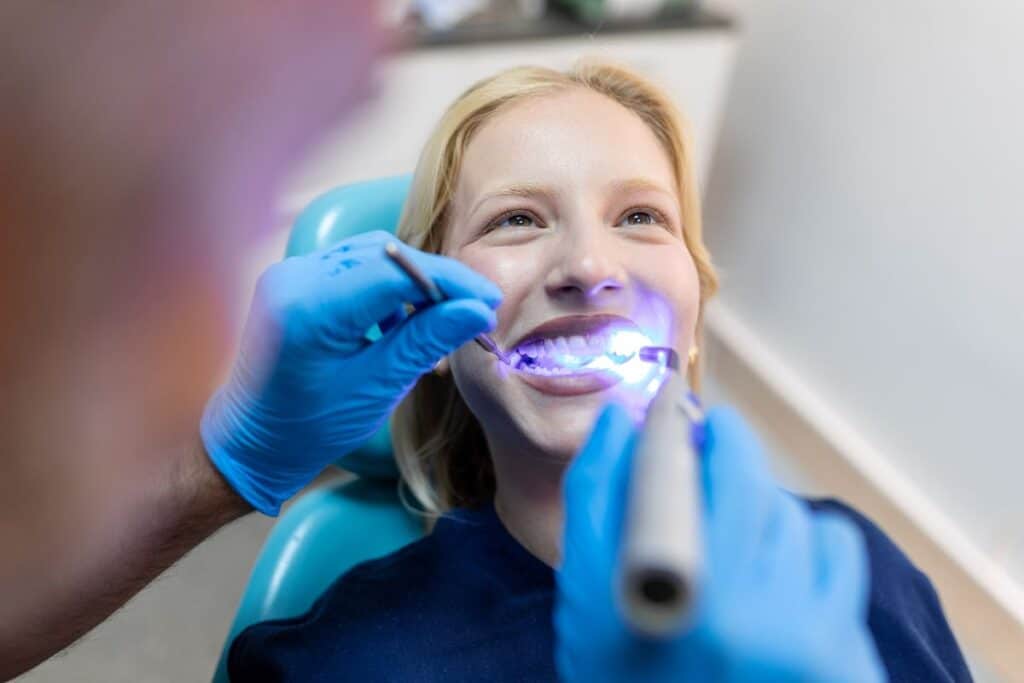 Dental professional using UV whitening light to treat patient's teeth during professional whitening procedure.