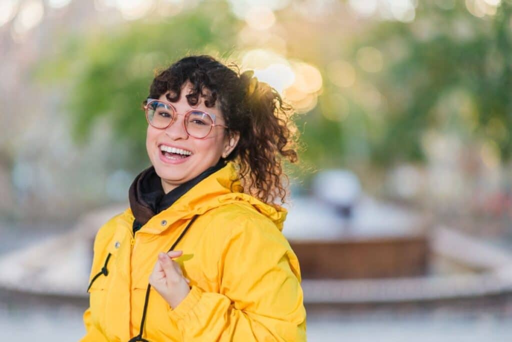 Happy woman in yellow jacket and glasses smiling outdoors on Valentine's Day.