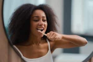 Woman brushing her teeth and smiling in a bright, modern dental office setting.