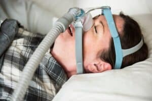 Woman wearing CPAP mask in bed for sleep apnea treatment.
