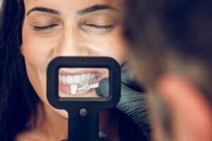 Dentist examining patient's tooth shade with porcelain veneer shade guide during cosmetic consultation.