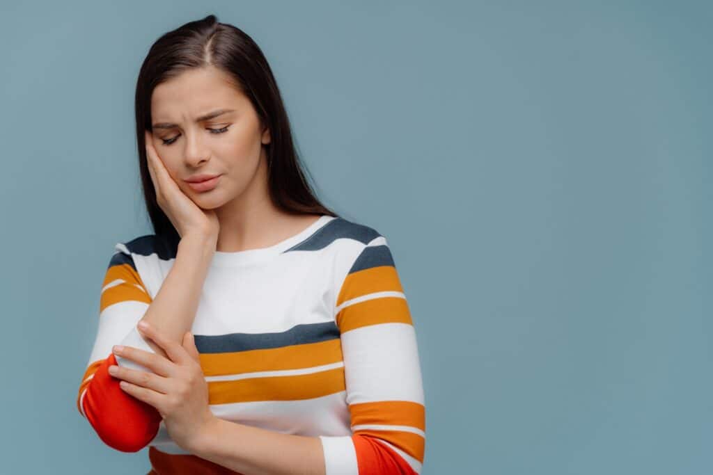 Woman holding her cheek in pain, illustrating dental discomfort management.