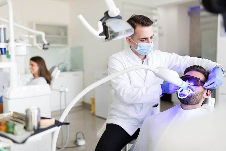 Dentist performing professional teeth whitening treatment on patient in modern dental office.