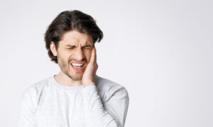 Man holding cheek in pain, expressing severe tooth discomfort requiring emergency dental treatment.