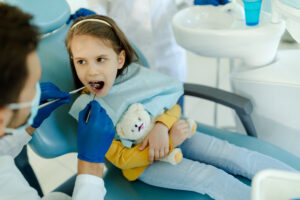 Young girl receiving dental examination in treatment chair, holding comfort toy.
