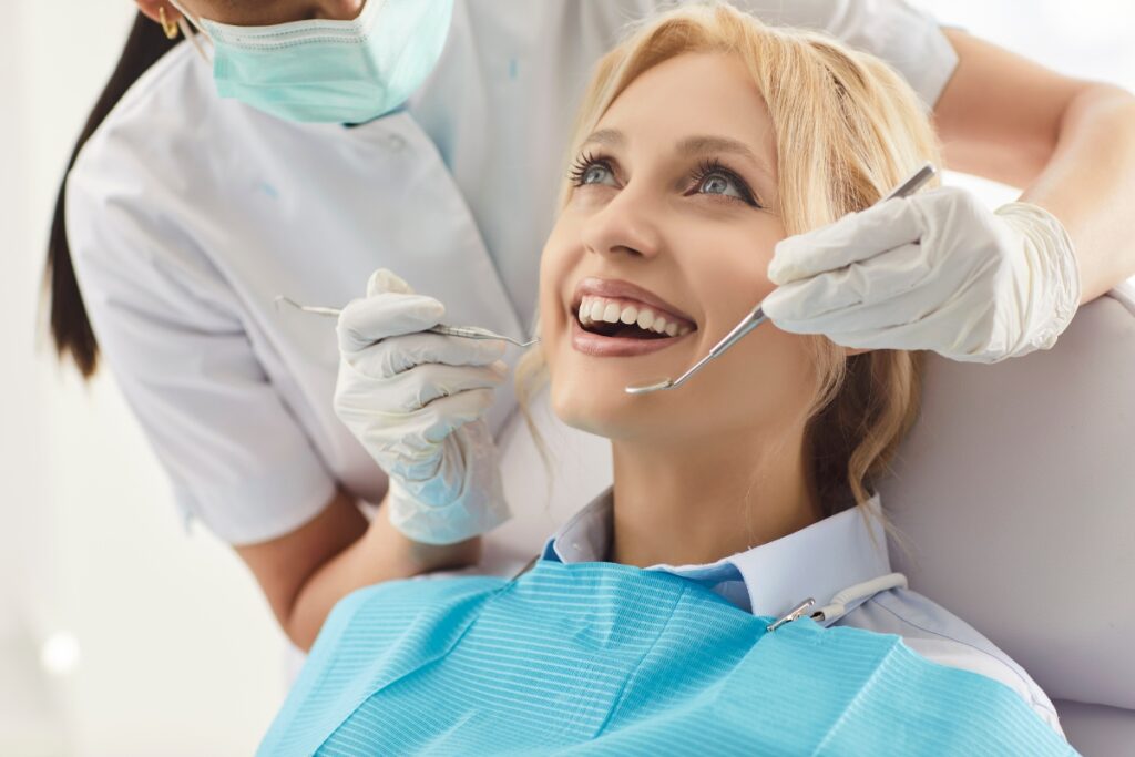 Smiling patient receiving dental examination from dentist wearing mask and gloves.
