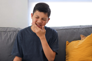 Young patient holding cheek in pain from severe toothache, experiencing dental distress.
