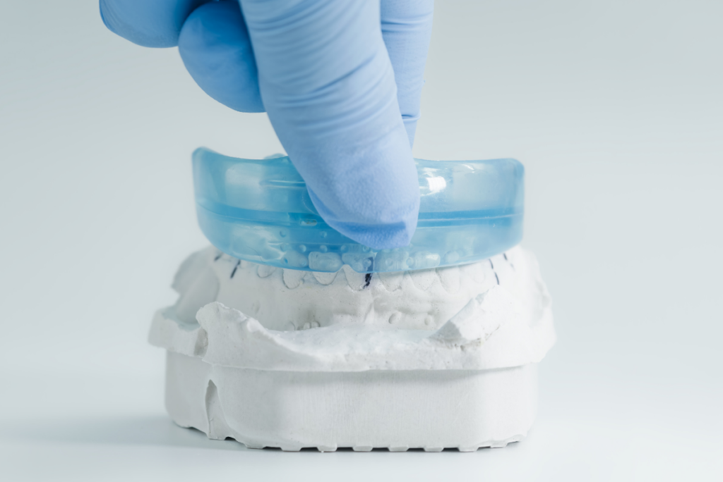 Dentist demonstrating mouthguard placement on dental model to prevent sports injuries.