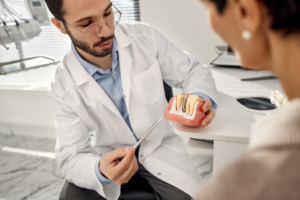 Dentist discussing dental implant model with patient during consultation.
