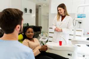 Female dentist in white coat smiling at patient during routine dental checkup in modern office.