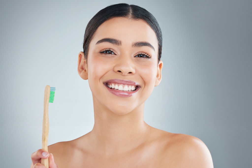 Young woman smiling while holding a natural wooden toothbrush with green bristles.