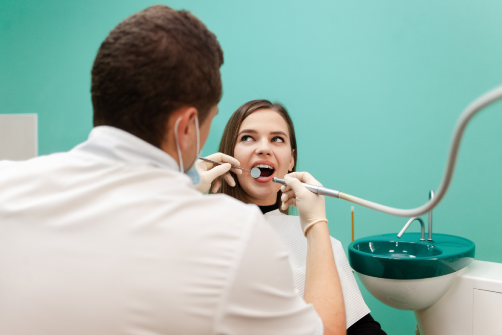 Dentist examining young patient's teeth during routine dental checkup in treatment room.