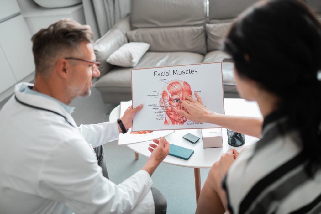 Male dentist explaining facial muscles diagram to female patient in consultation.
