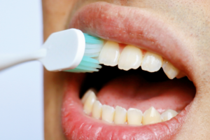Person using an electric toothbrush on upper teeth, demonstrating proper brushing technique for dental care.