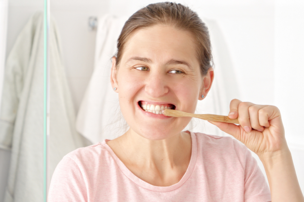 Woman brushing her teeth with a wooden toothbrush and smiling brightly.