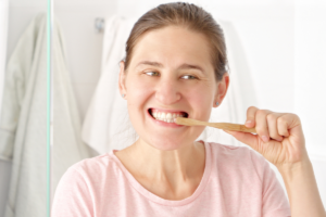 Woman brushing her teeth with a wooden toothbrush and smiling brightly.